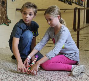 students kneeling on floor in school hallway while launching a catapult made of popsicle sticks