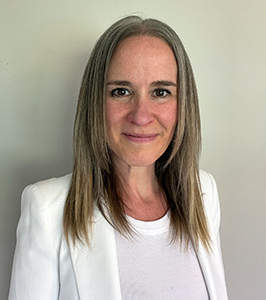 Harry Hoag Elementary School Acting Principal, Amy Bartholomew, who has long dark blond hair and is wearing a white top and blazer, looks at and smiles for the camera.