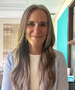 Harry Hoag Elementary School Principal, Amy Bartholomew, who has long dark blond hair and is wearing a white top and blazer, looks at and smiles for the camera.